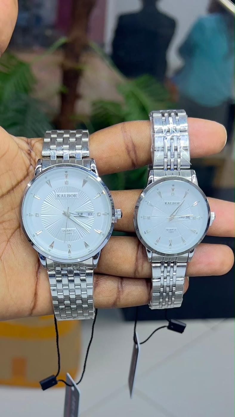 Two steel watches held in a hand with their price tags still attached